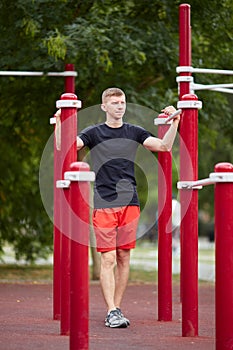 Young strong man does pull-ups on a horizontal bar on a sports ground in the summer in the city.