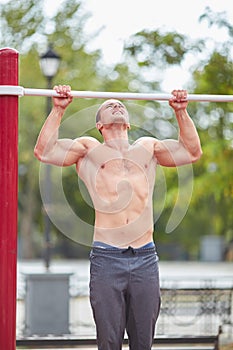 Young strong man does pull-ups on a horizontal bar on a sports ground in the summer in the city.