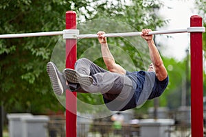 Young strong man does pull-ups on a horizontal bar on a sports ground in the summer in the city.