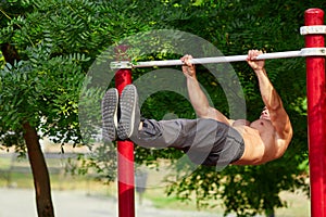 Young strong man does pull-ups on a horizontal bar on a sports ground in the summer in the city.