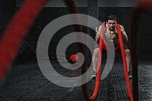 Young strong man doing battle ropes exercise at the crossfit gym