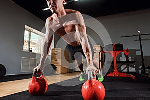 Young strong man doing push-ups on kettlebells