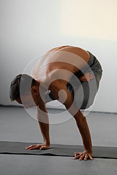 A young strong man doing yoga exercises - handstand or asana Urdhva Kukkutasana.