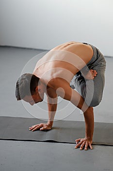 A young strong man doing yoga exercises - handstand or asana Urdhva Kukkutasana.