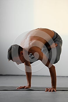 A young strong man doing yoga exercises - handstand or asana Urdhva Kukkutasana.