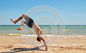 Young strong man in excellent physical shape handstands on the beach near the sea