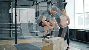 Young strong man jumping on wooden box working out with crossfit trainer in gym