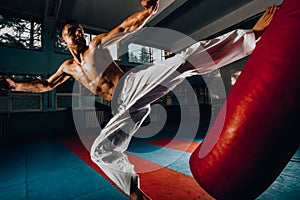 Young strong man kicking punching bag during his training