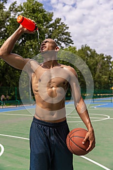 Young strong man, male basketball player training at street public stadium, sport court or palyground outdoors. Concept