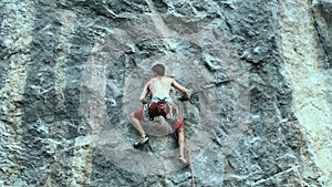 Young strong man rock climber carefully climbing on a cliff, searching, reaching and gripping hold.