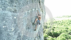 Young strong man rock climber climbing on a vertical limestone cliff, attaching rope and finishing route