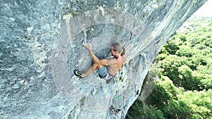 Young strong man rock climber climbing on a vertical limestone cliff, attaching rope and finishing route