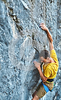 Young strong man rock climber in yellow t-shirt, climbing on a cliff