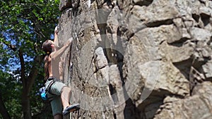 Young strong man rockclimber climbing on a granite cliff, reaching and gripping hold.