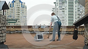 Young strong man smashes the monitor with a sledgehammer on the roof. Hammer, bat, violence, hatred, anarchy