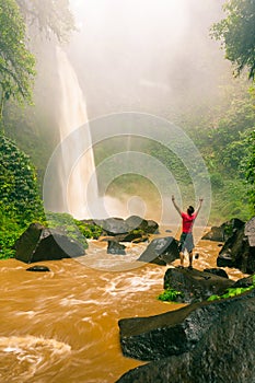 Young strong man traveler enjoy spectacular morning view, beautiful Nungnung Waterfall, Indonesia