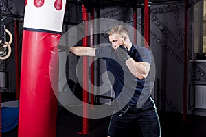 Young strong mixed martial arts fighter delivers strong hand punch to punching bag. Active exercise in gym.