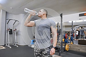 Young strong muscular man in gym drinking water from bottle