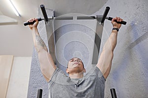 Young strong muscular man in gym, male exercising, doing pull ups