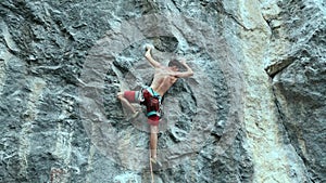 Young strong muscular man rock climber carefully climbing on a high vertical limestone cliff, trying to hang and falling