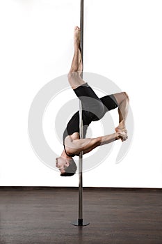 Young strong pole dancer smiling man in black clothes on pylon. White background