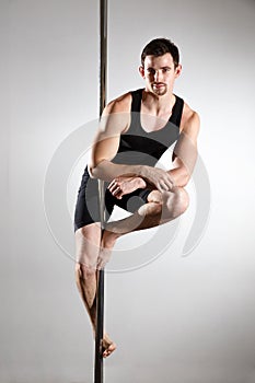 Young strong pole dancer smiling man in black clothes on pylon. White background