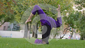 Young strong sporty woman in hijab and purple pants top practicing outdoors, girl trainer doing supported headstand