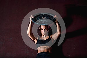 Young strong sweaty fit muscular girl with big muscles doing sit ups with barbell weight plate for abdominal muscles or abs hard c