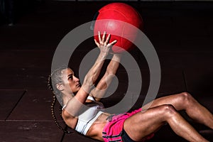 Young strong sweaty fit muscular girl with big muscles doing sit ups with medicine ball for abdominal muscles or abs hard workout