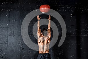 Young strong sweaty focused fit muscular man with big muscles doing throwing medicine ball up on the wall for training hard core w