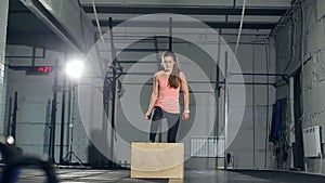 Young strong woman with perfect fitness body in sportswear doing set of box jumps at the gym. Girl jumping into wooden