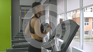 Young strong woman with perfect fitness body in sportswear running on treadmill in gym. Girl exercising during cardio