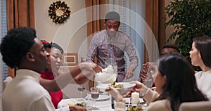 Young student of African appearance invited friends to birthday party. Guy in shirt is standing at table and cutting