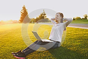 Young student brunette female in casual clothes. Woman sitting, relaxing, hands behind head. laptop pc computer on green