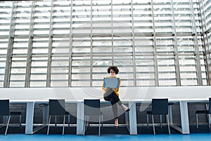 Young student or businesswoman sitting on desk in room in a library or office, using laptop.