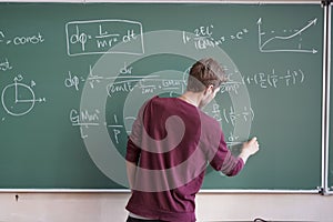 Young student in casual writing physics formula on the blackboard during study course s