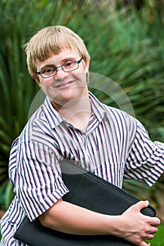 Young student with down syndrome holding files outdoors.