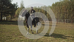 A young student of an equestrian riding school trains in an open-air paddock, riding a spotted horse. In slowmotion