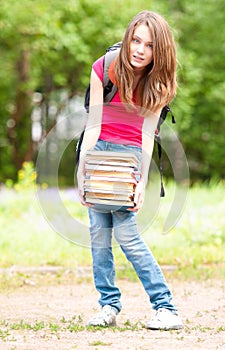 Young student girl holding big pile of heavy books