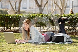 Young student girl lying on park grass with computer studying or surfing on internet