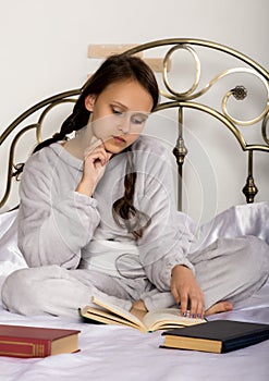 Young student girl reads a book while lying on a bed doing homework