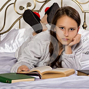 Young student girl reads a book while lying on a bed doing homework