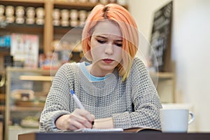 Young student girl schoolgirl writer makes notes in his notebook