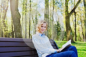 Young student girl in shirt sitting with a book in her hand in a green park, science and education, reading