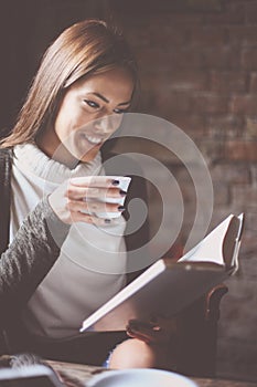 Young student girl sitting in cafe reading book and hol