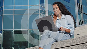 Young student girl using laptop sitting outside in city. Beautiful business woman with computer having online video chat