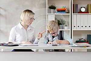 A young student and his confident-looking teacher sit at the table and write a dictation.