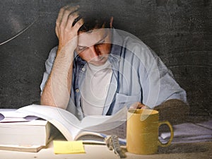 Young student at home desk reading studying at night with pile of books and coffee