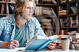 Young student in library at desk look away handwrite in notebook.