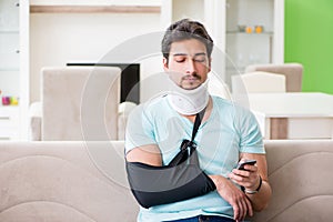 The young student man with neck and hand injury sitting on the sofa